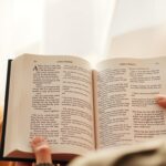 Person praying with Bible open to Luke's Gospel featuring the Lord's Prayer for Seventeenth Sunday in Ordinary Time, Cycle C